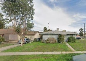 Fresno, CA home bought by Varo as-is: single-story gray ranch-style house with a lawn and shrubs